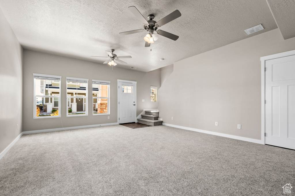 Empty room with ceiling fan, dark colored carpet, and a textured ceiling