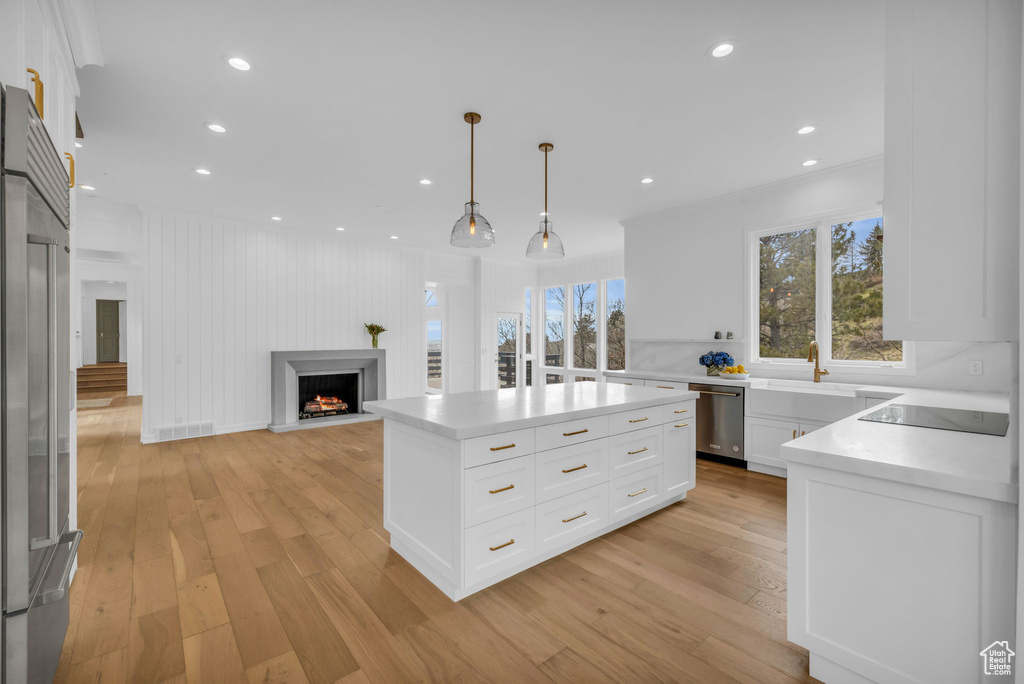 Kitchen featuring white cabinetry, light hardwood / wood-style flooring, appliances with stainless steel finishes, and pendant lighting