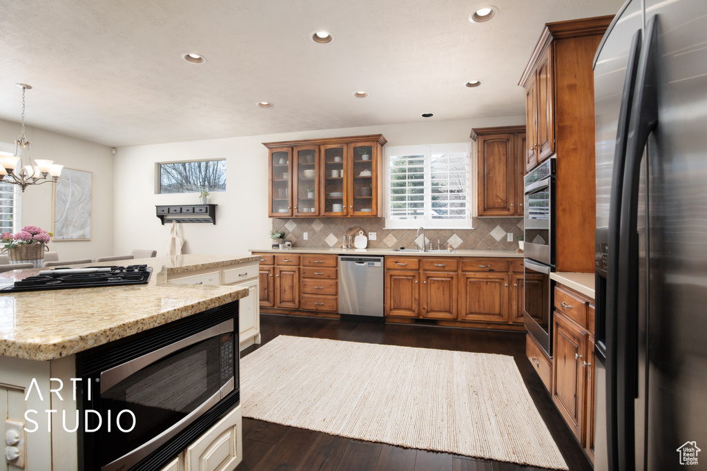 Kitchen featuring decorative light fixtures, appliances with stainless steel finishes, tasteful backsplash, dark hardwood / wood-style floors, and sink