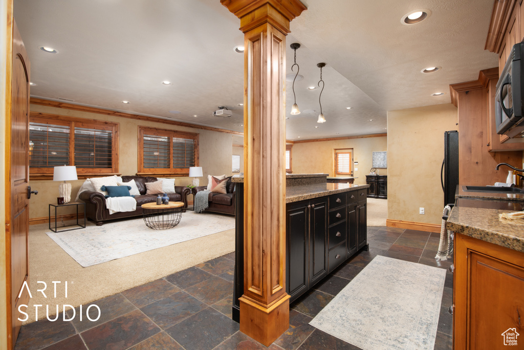 Kitchen featuring ornate columns, black refrigerator, pendant lighting, light stone countertops, and dark tile flooring