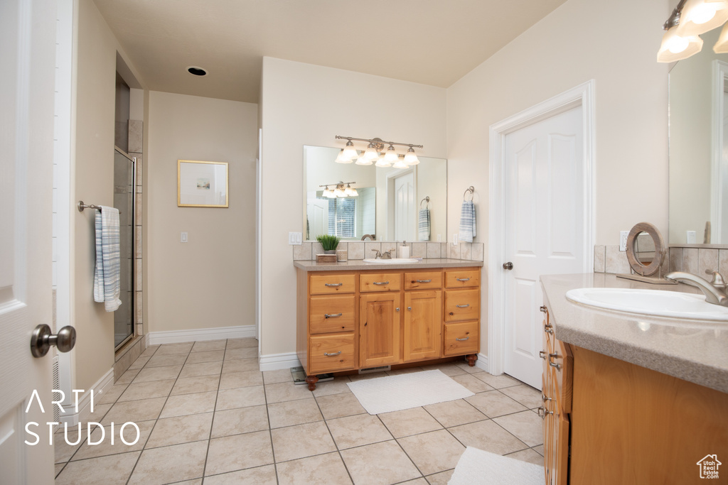 Bathroom featuring a shower with shower door, dual sinks, oversized vanity, and tile flooring