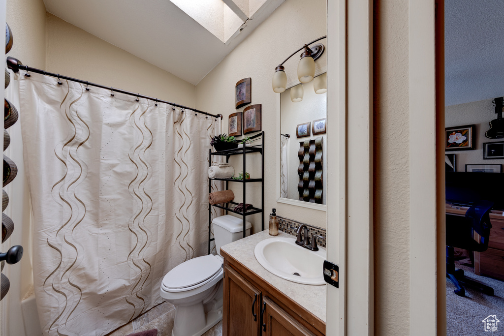 Bathroom featuring toilet, vanity, and vaulted ceiling with skylight
