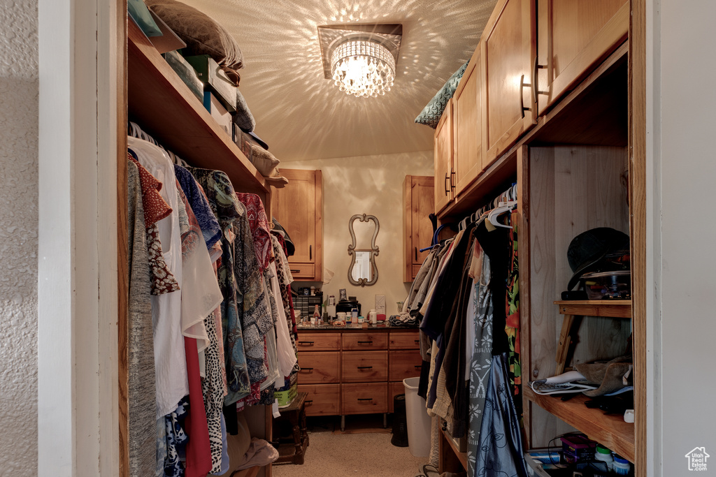 Walk in closet with light colored carpet and a notable chandelier