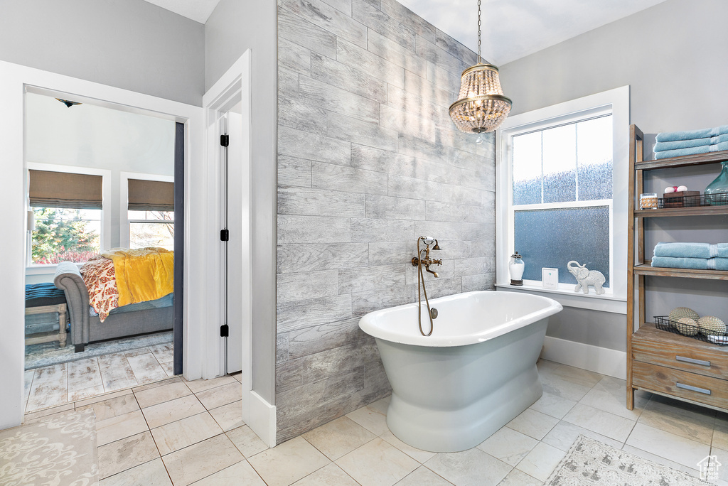 Bathroom featuring tile walls, a bath to relax in, tile floors, and an inviting chandelier