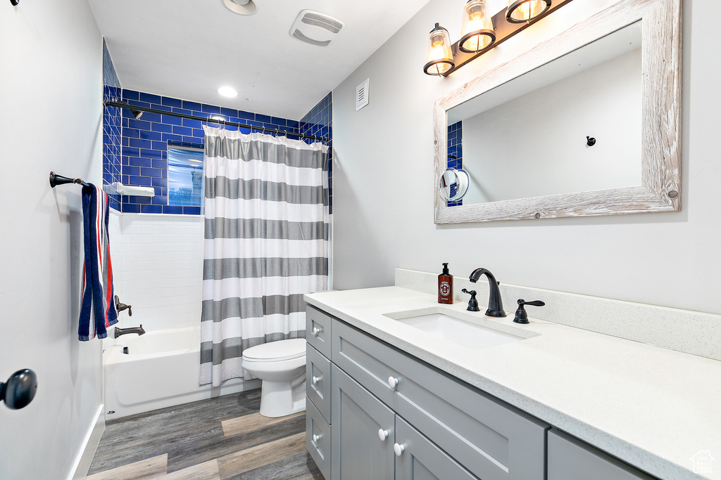 Full bathroom with oversized vanity, toilet, wood-type flooring, and shower / bathtub combination with curtain