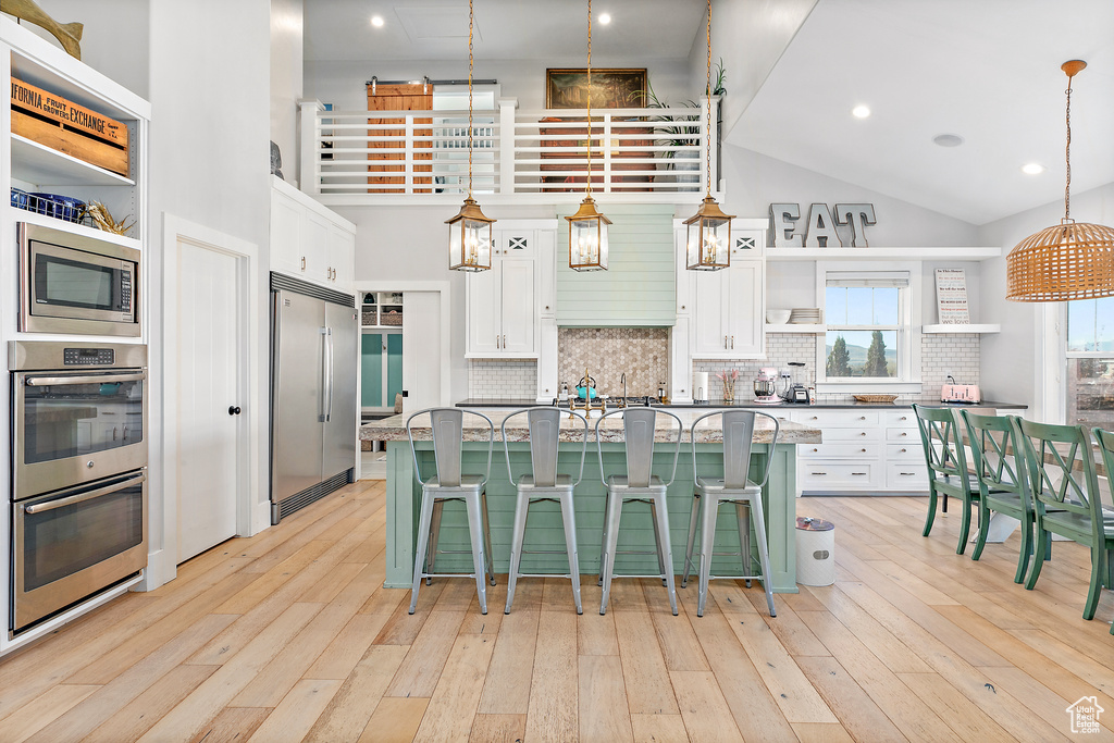 Kitchen with high vaulted ceiling, white cabinetry, a breakfast bar, and built in appliances