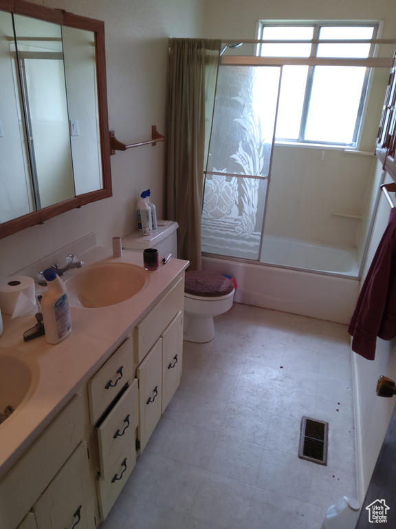 Full bathroom with shower / bath combination with glass door, tile flooring, toilet, vanity with extensive cabinet space, and double sink