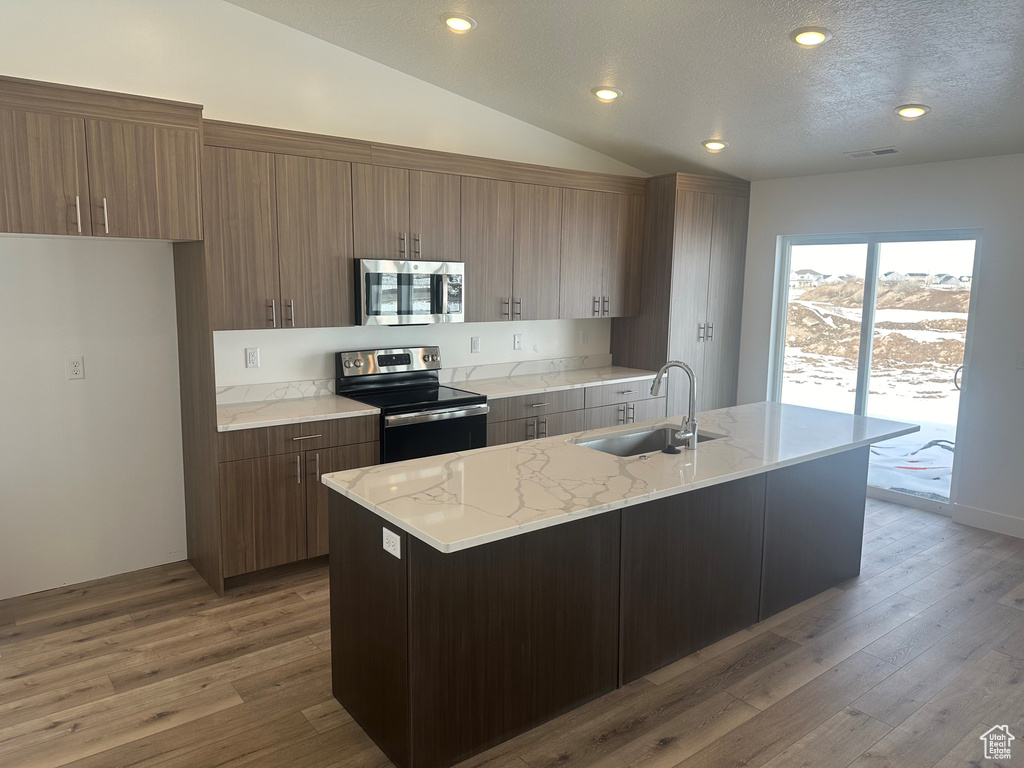 Kitchen featuring a center island with sink, appliances with stainless steel finishes, hardwood / wood-style floors, and vaulted ceiling