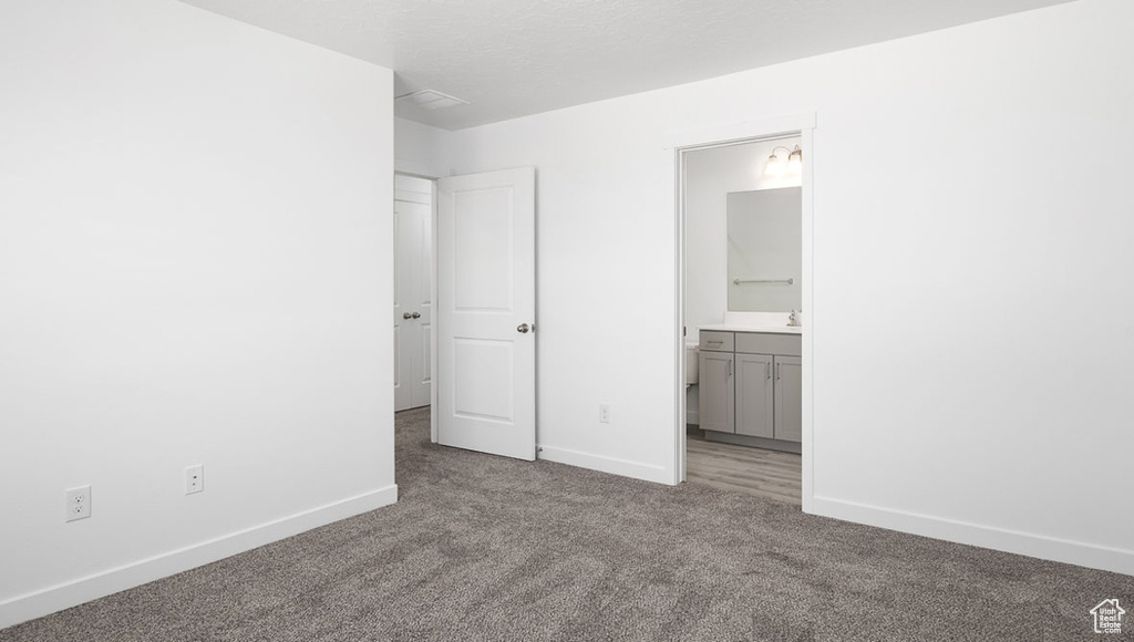 Unfurnished bedroom with dark carpet and connected bathroom