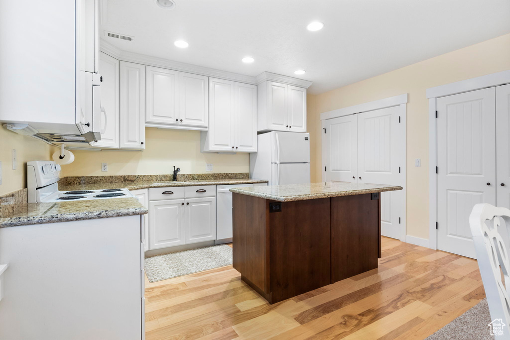 Kitchen featuring light stone counters, light hardwood / wood-style floors, white cabinets, white appliances, and sink