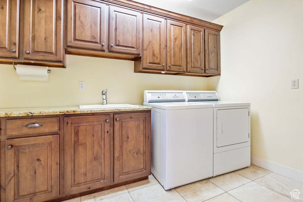 Clothes washing area featuring sink, cabinets, washer and clothes dryer, and light tile floors