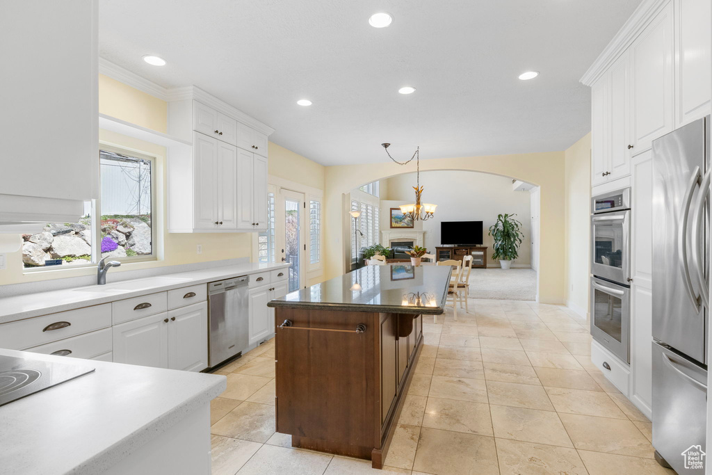 Kitchen with an inviting chandelier, white cabinetry, light tile floors, stainless steel appliances, and a center island