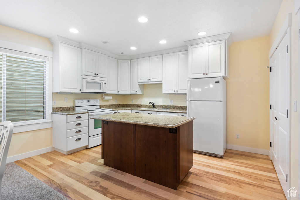 Kitchen featuring white cabinets, a center island, white appliances, light stone counters, and light wood-type flooring
