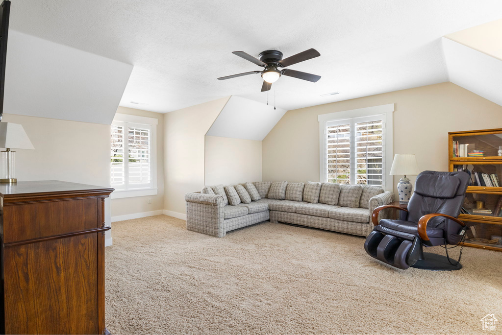 Living room with vaulted ceiling, light colored carpet, ceiling fan, and plenty of natural light