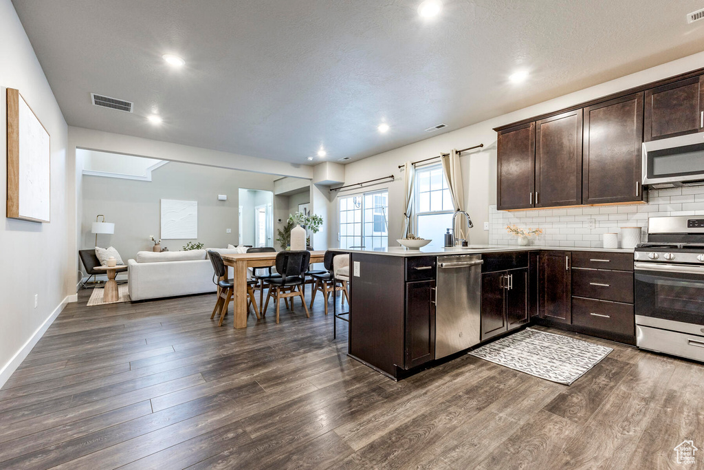 Kitchen with backsplash, dark wood-type flooring, dark brown cabinetry, and stainless steel appliances