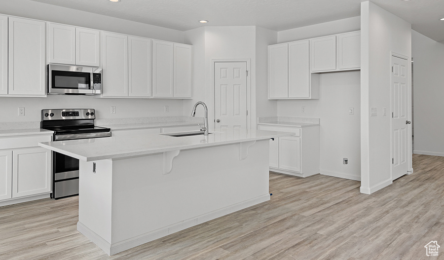 Kitchen with appliances with stainless steel finishes, white cabinetry, a center island with sink, light wood-type flooring, and sink