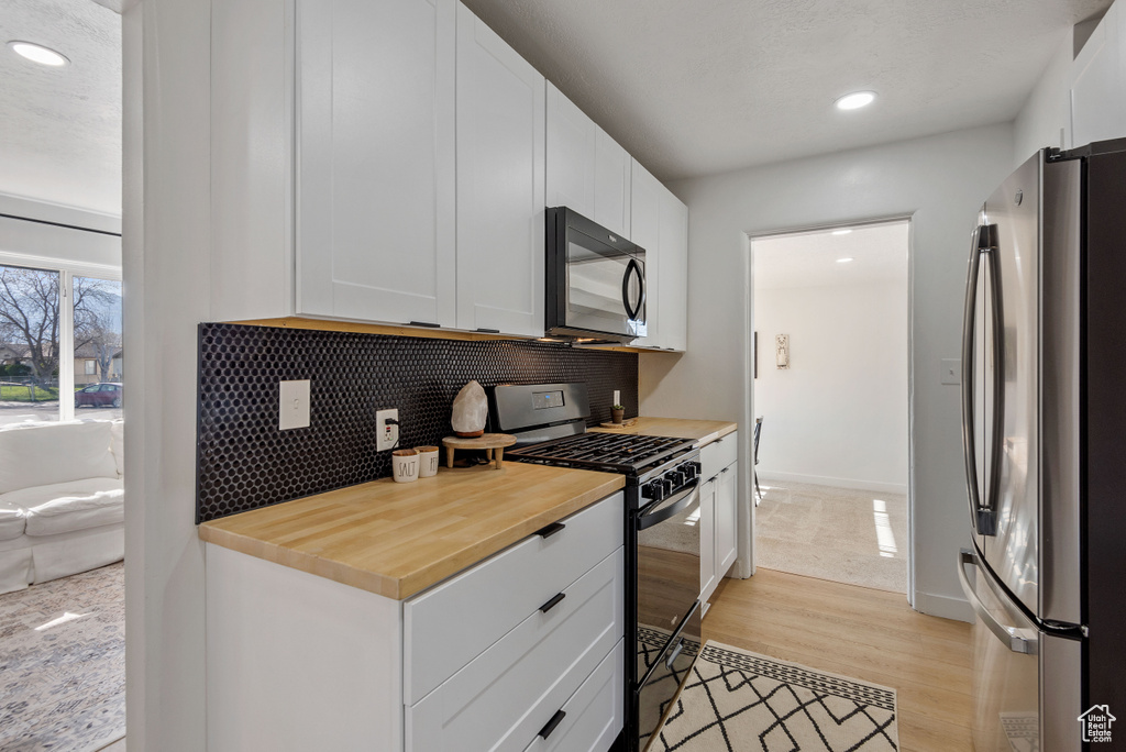 Kitchen with white cabinets, stainless steel fridge, gas range oven, light hardwood / wood-style floors, and tasteful backsplash