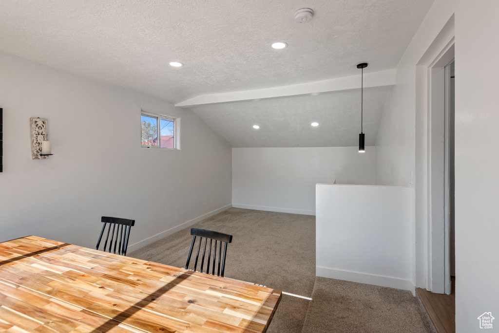 Unfurnished dining area with a textured ceiling, lofted ceiling, and dark colored carpet