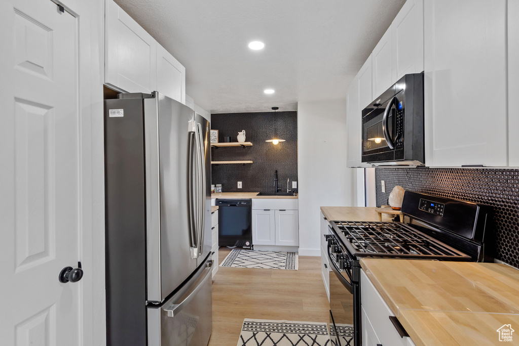 Kitchen featuring light hardwood / wood-style flooring, tasteful backsplash, black appliances, and white cabinets