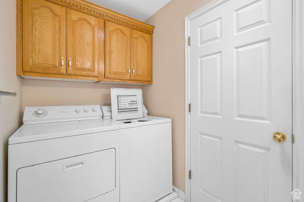 Clothes washing area featuring washing machine and clothes dryer and cabinets