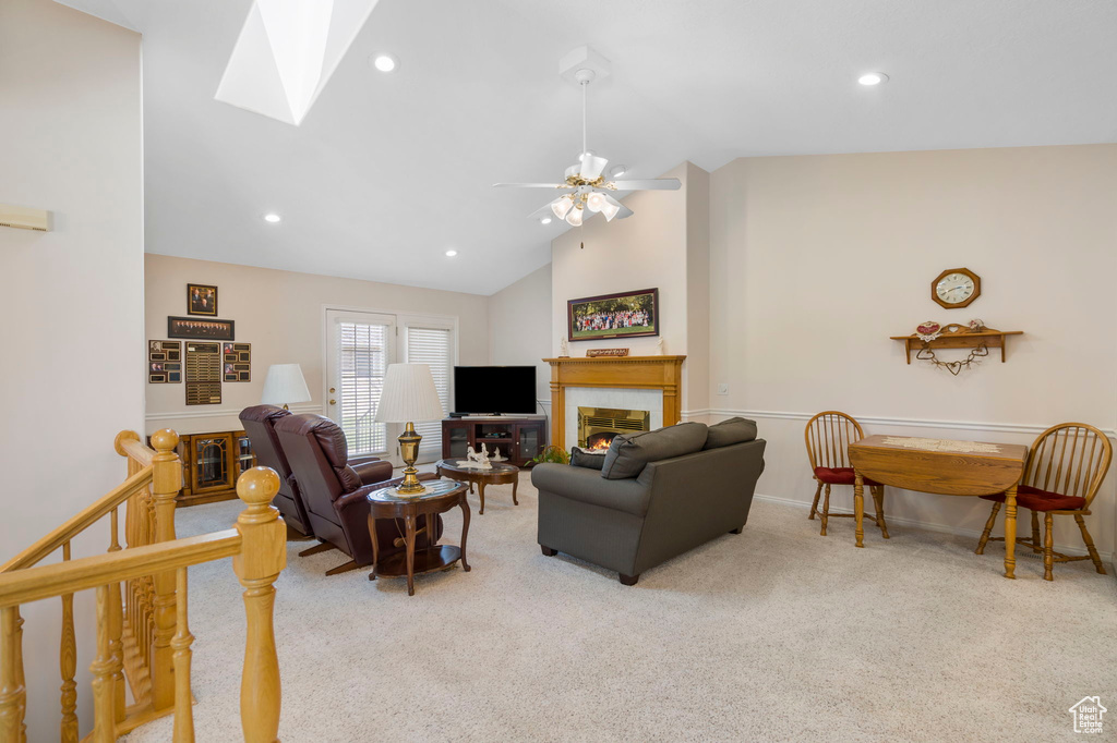Living room featuring ceiling fan, high vaulted ceiling, light carpet, and a skylight