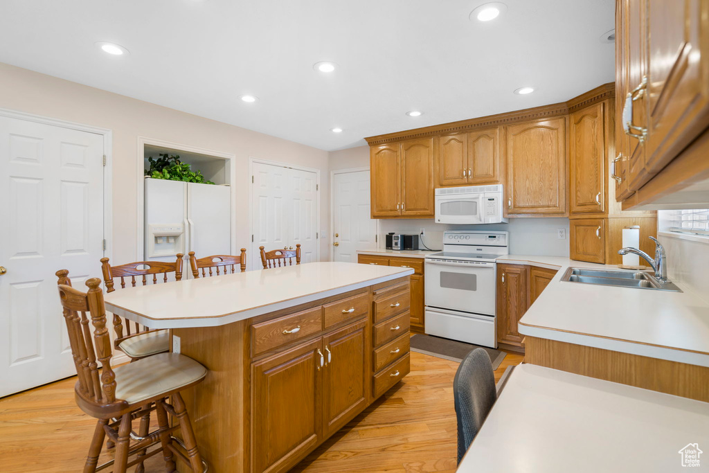 Kitchen featuring sink, a kitchen breakfast bar, light hardwood / wood-style floors, white appliances, and a kitchen island