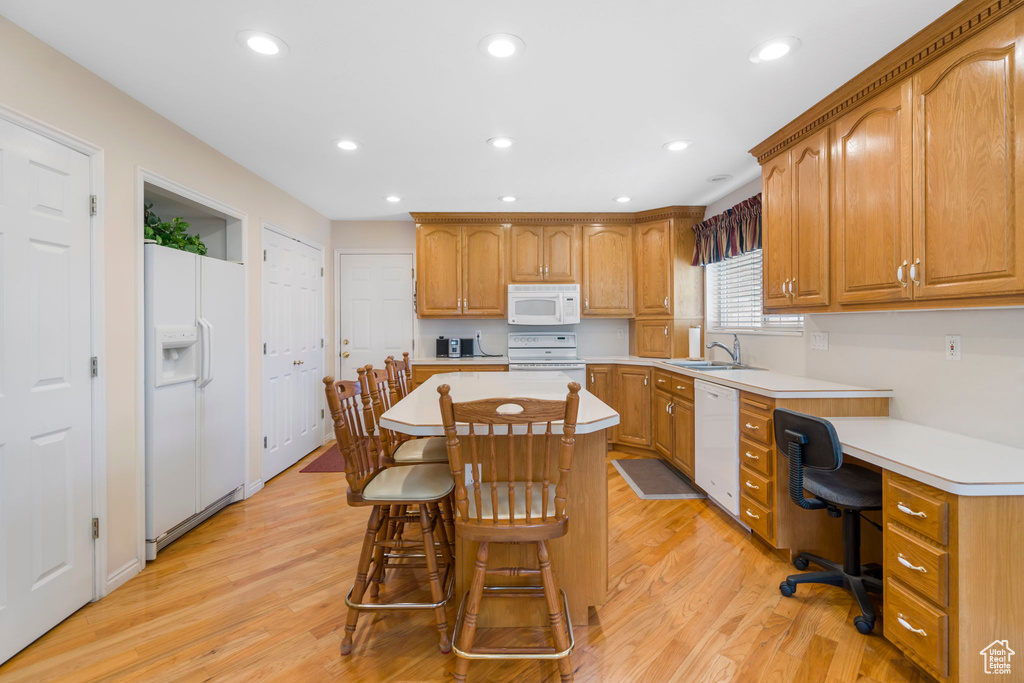 Kitchen with white appliances, light hardwood / wood-style flooring, a center island, and a kitchen breakfast bar