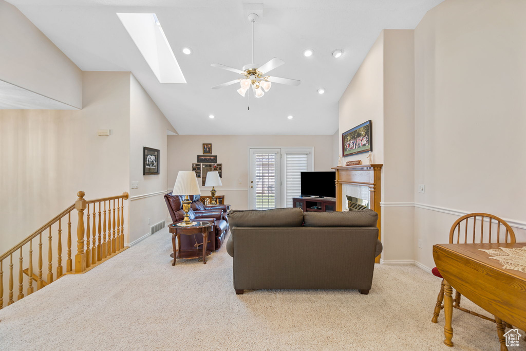 Carpeted living room with a skylight, ceiling fan, and high vaulted ceiling