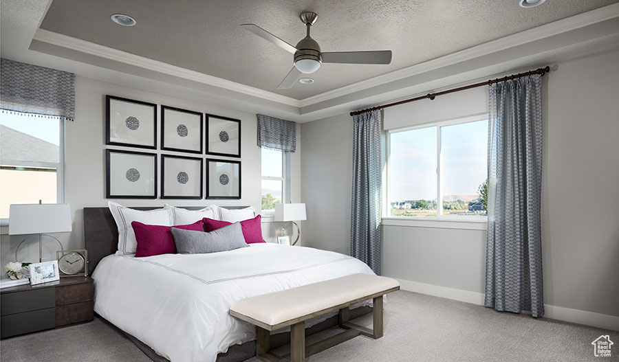 Carpeted bedroom featuring a textured ceiling, ceiling fan, a raised ceiling, and crown molding