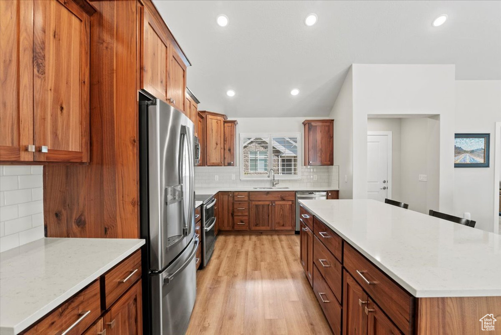 Kitchen with appliances with stainless steel finishes, light wood-type flooring, light stone counters, backsplash, and sink