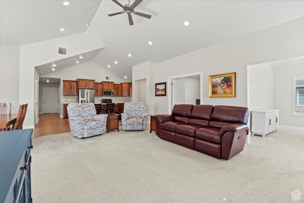 Living room with ceiling fan, light colored carpet, and high vaulted ceiling