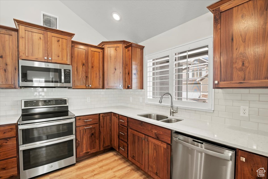 Kitchen featuring light hardwood / wood-style floors, stainless steel appliances, backsplash, lofted ceiling, and sink