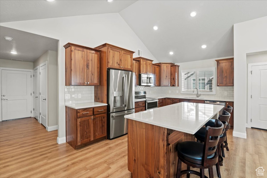 Kitchen featuring backsplash, stainless steel appliances, light wood-type flooring, and a kitchen island