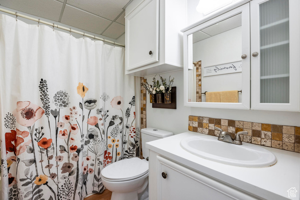 Bathroom featuring a drop ceiling, backsplash, toilet, and large vanity
