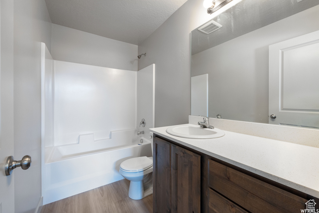 Full bathroom featuring toilet, vanity, hardwood / wood-style floors, a textured ceiling, and bathing tub / shower combination