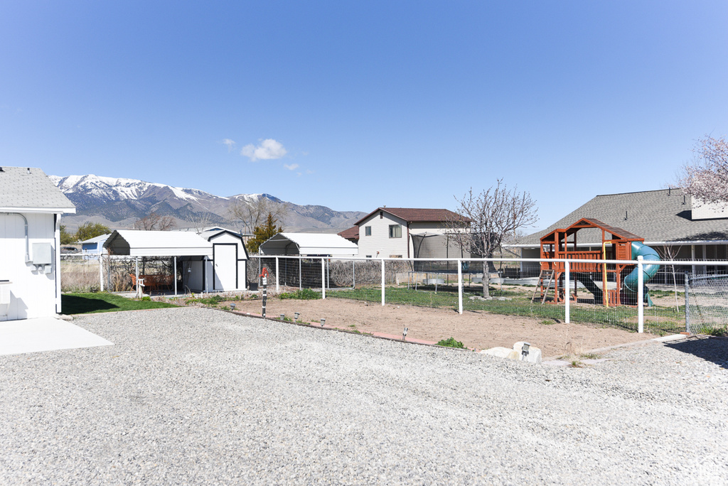 View of front of house with a playground, a mountain view, and a storage unit