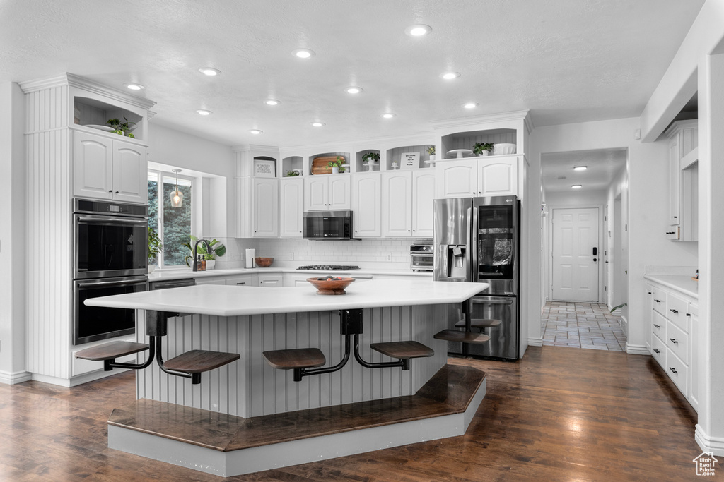 Kitchen with a kitchen island, dark wood-type flooring, appliances with stainless steel finishes, and a breakfast bar