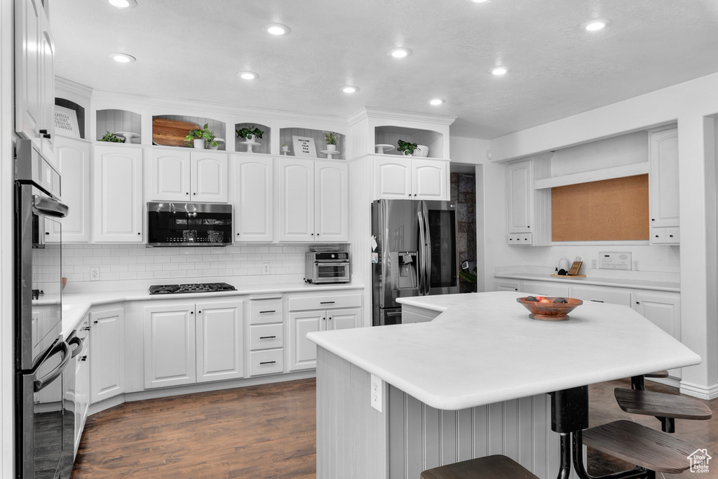 Kitchen with dark wood-type flooring, appliances with stainless steel finishes, tasteful backsplash, white cabinets, and a kitchen breakfast bar