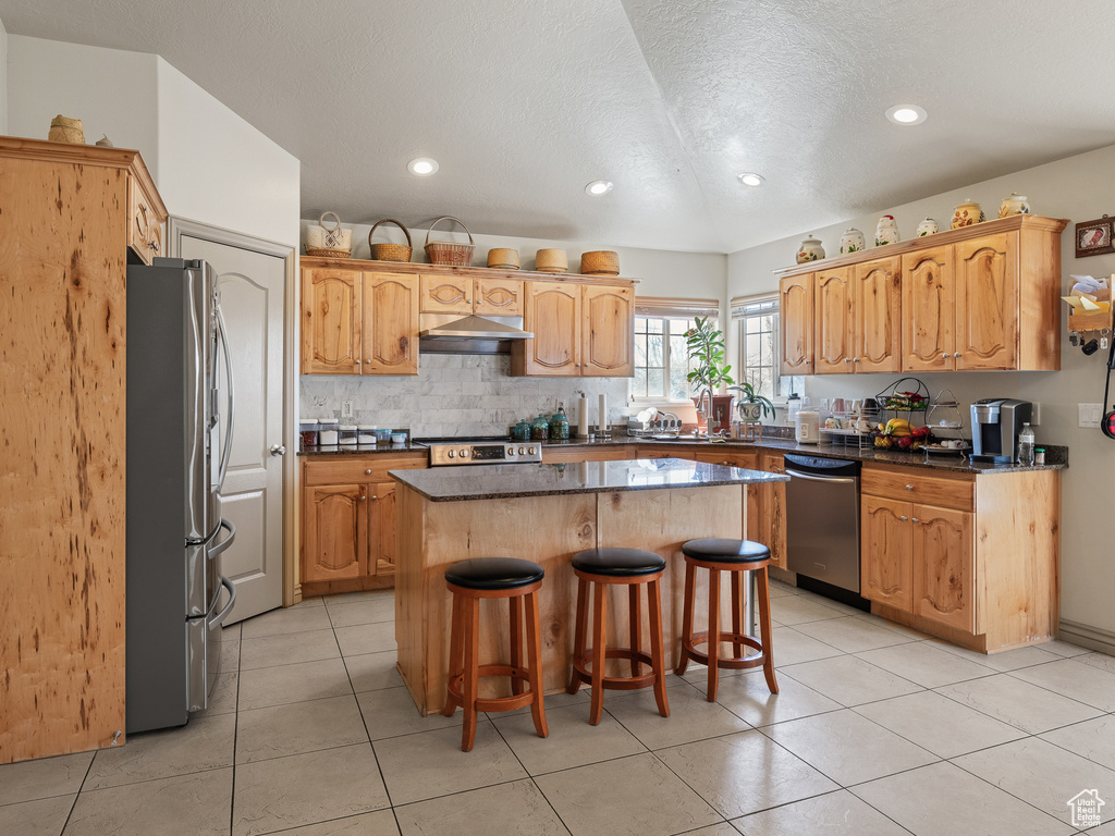 Kitchen featuring appliances with stainless steel finishes, a center island, a kitchen bar, and light tile floors
