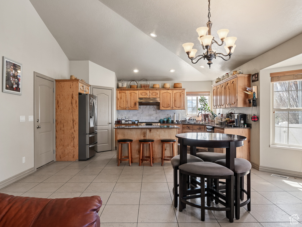Kitchen with a kitchen island, a breakfast bar, backsplash, light tile floors, and stainless steel refrigerator with ice dispenser