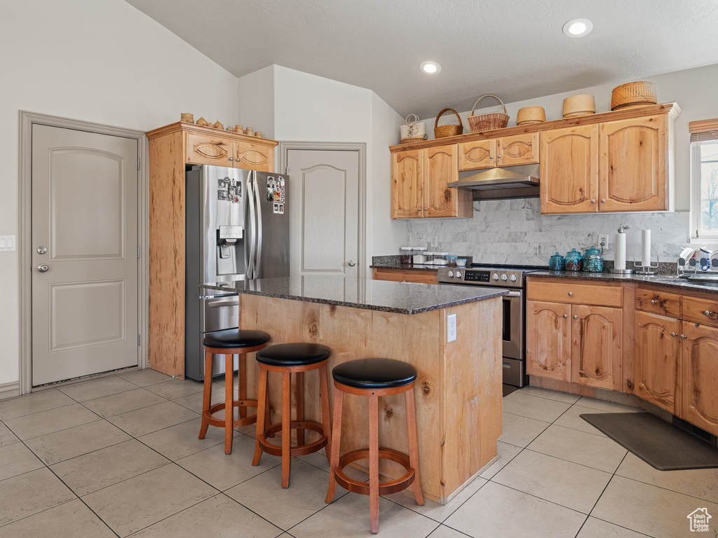 Kitchen with a kitchen island, a breakfast bar area, stainless steel appliances, dark stone countertops, and light tile floors