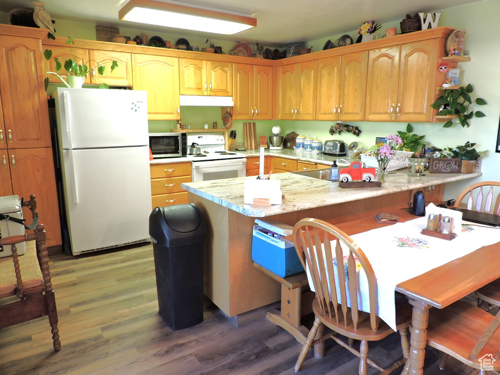 Kitchen featuring kitchen peninsula, white appliances, light wood-type flooring, and light stone countertops