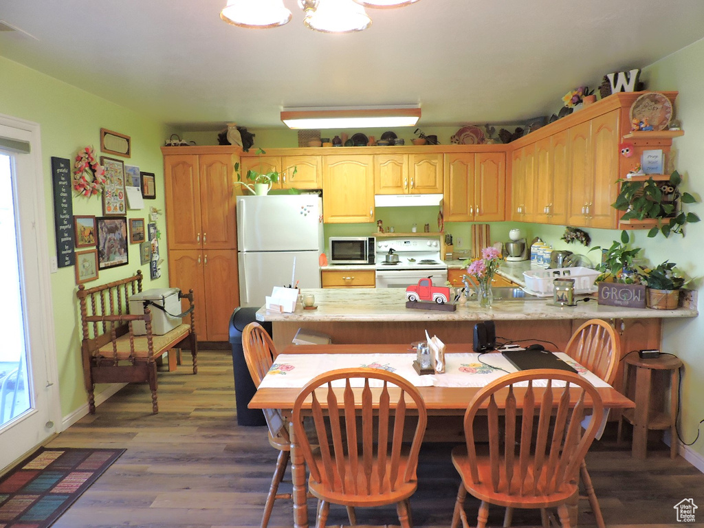 Kitchen featuring dark wood-type flooring, kitchen peninsula, a kitchen breakfast bar, light stone countertops, and white appliances