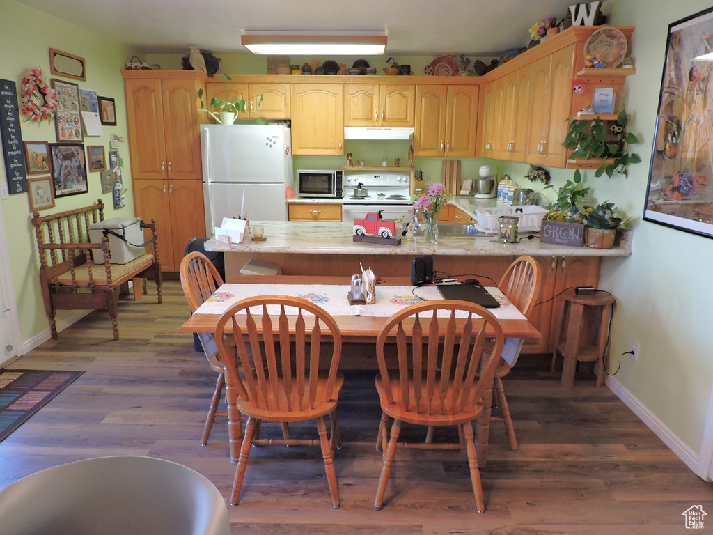 Kitchen featuring dark hardwood / wood-style flooring, white appliances, and a kitchen bar