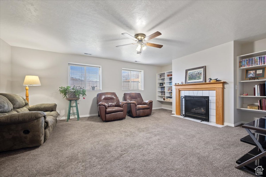 Living room with a textured ceiling, ceiling fan, carpet, and a fireplace