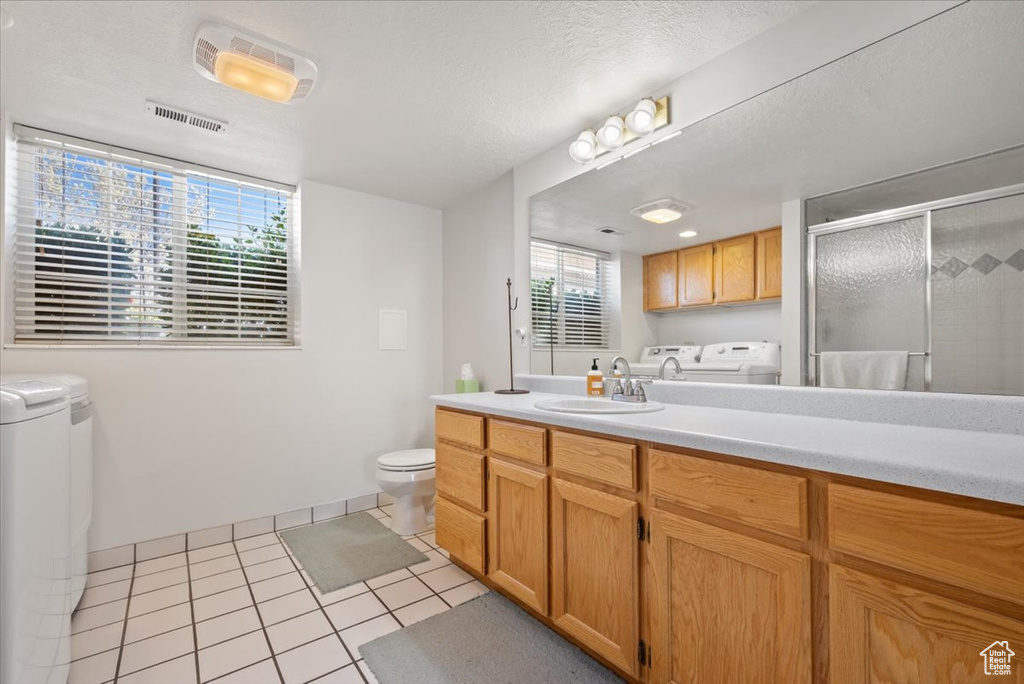 Bathroom featuring washing machine and clothes dryer, tile flooring, a textured ceiling, toilet, and vanity with extensive cabinet space