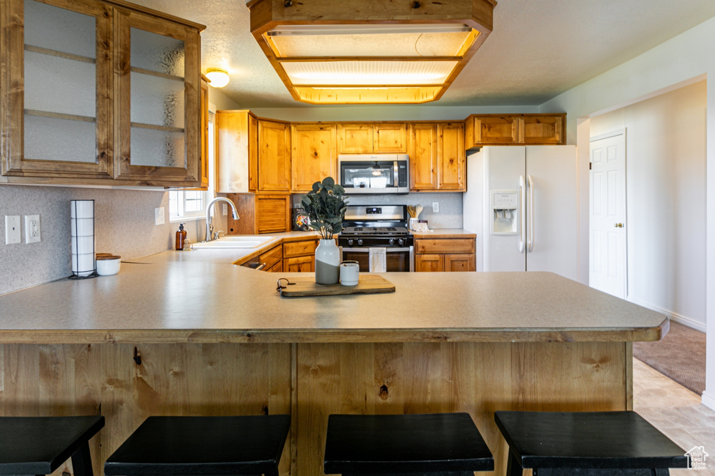 Kitchen featuring stainless steel appliances, kitchen peninsula, sink, a breakfast bar, and light tile flooring