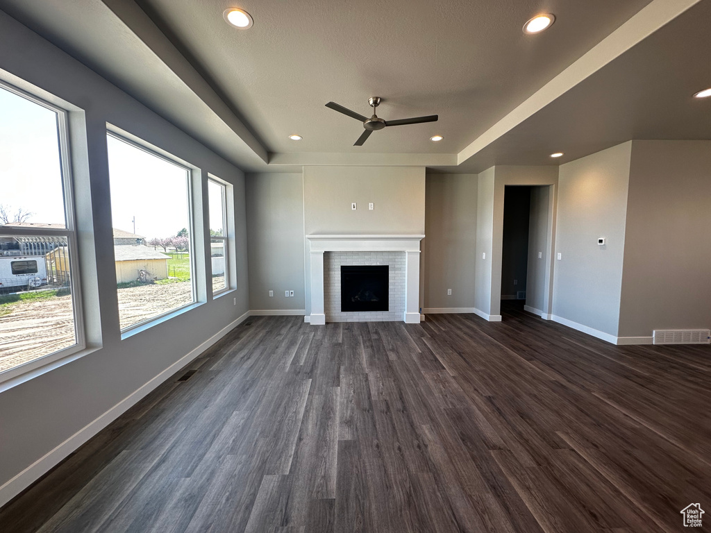 Unfurnished living room with dark hardwood / wood-style floors, ceiling fan, a brick fireplace, and a tray ceiling