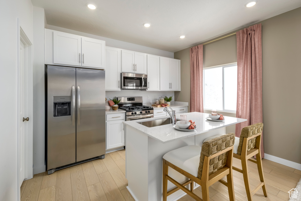 Kitchen featuring appliances with stainless steel finishes, a kitchen breakfast bar, white cabinetry, light wood-type flooring, and a center island with sink
