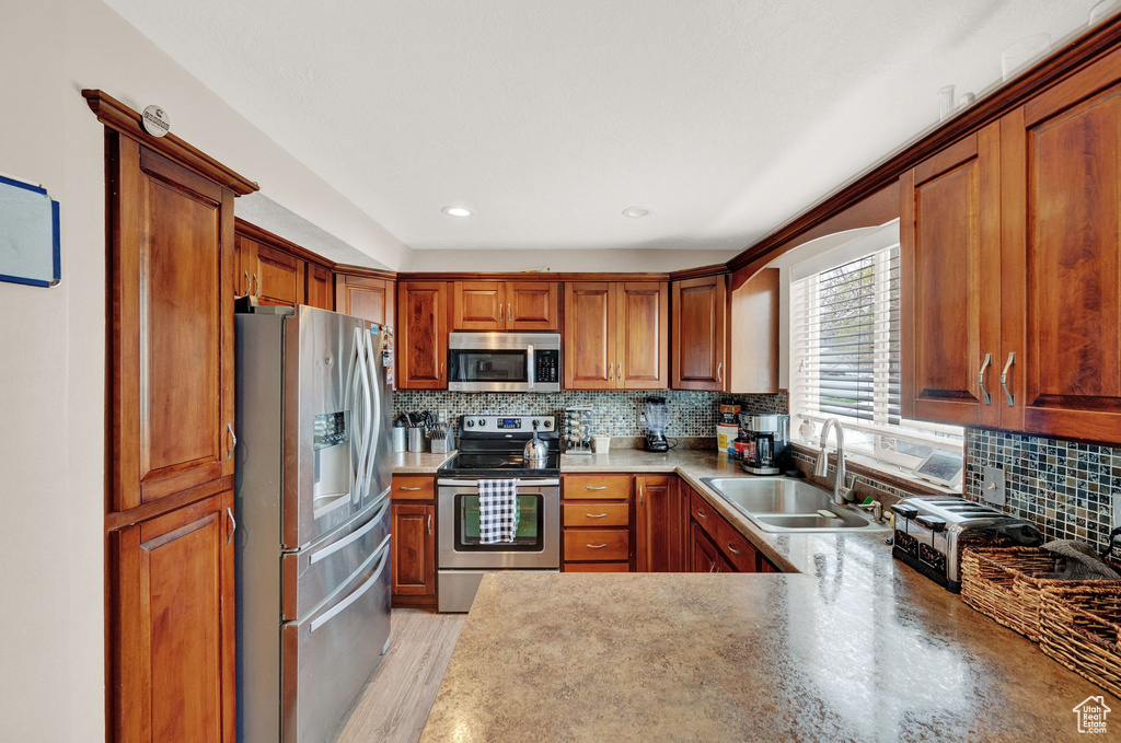 Kitchen with appliances with stainless steel finishes, light wood-type flooring, backsplash, sink, and kitchen peninsula